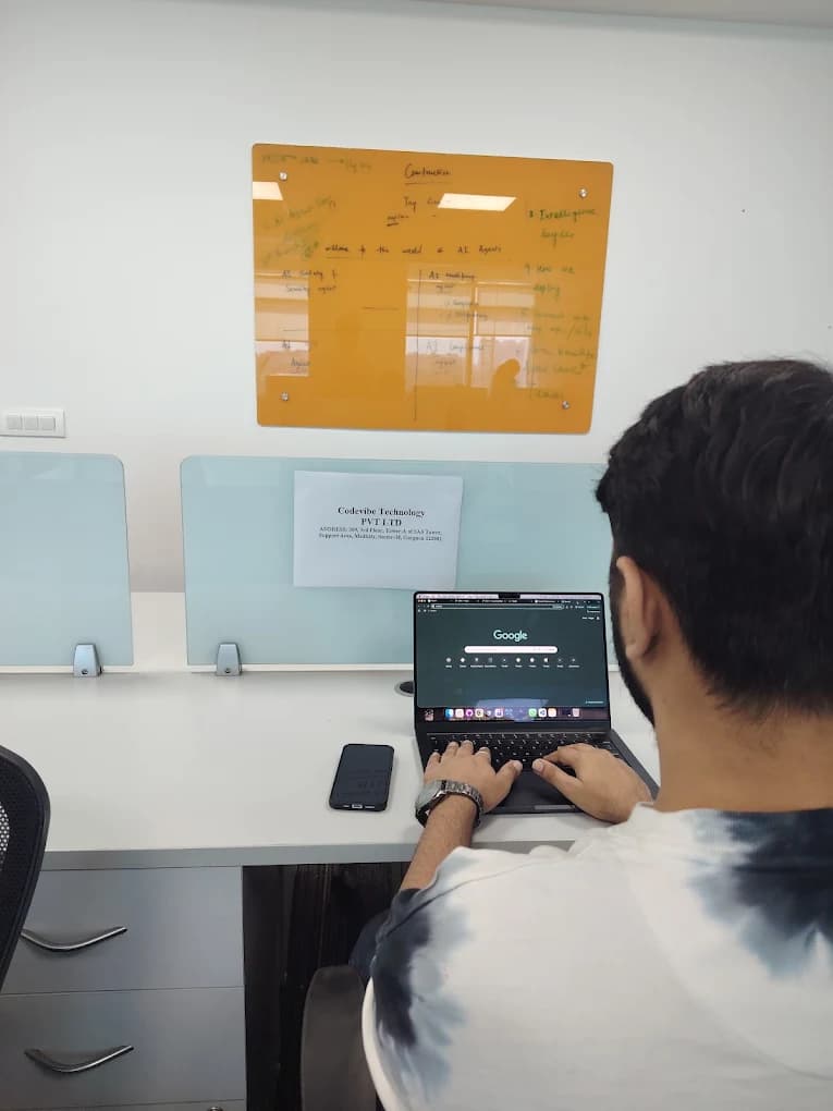 A Codevibe engineer working at a laptop beside a whiteboard of AI architecture notes, in the Gurugram office